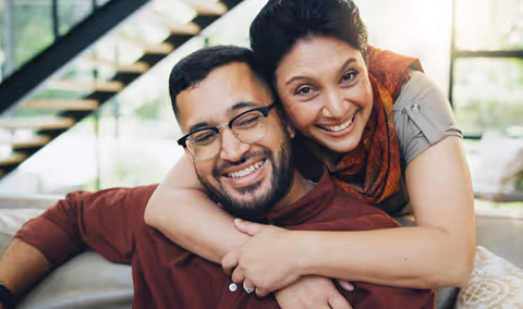 Smiling woman hugging a man wearing glasses warmly on a sofa indoors.